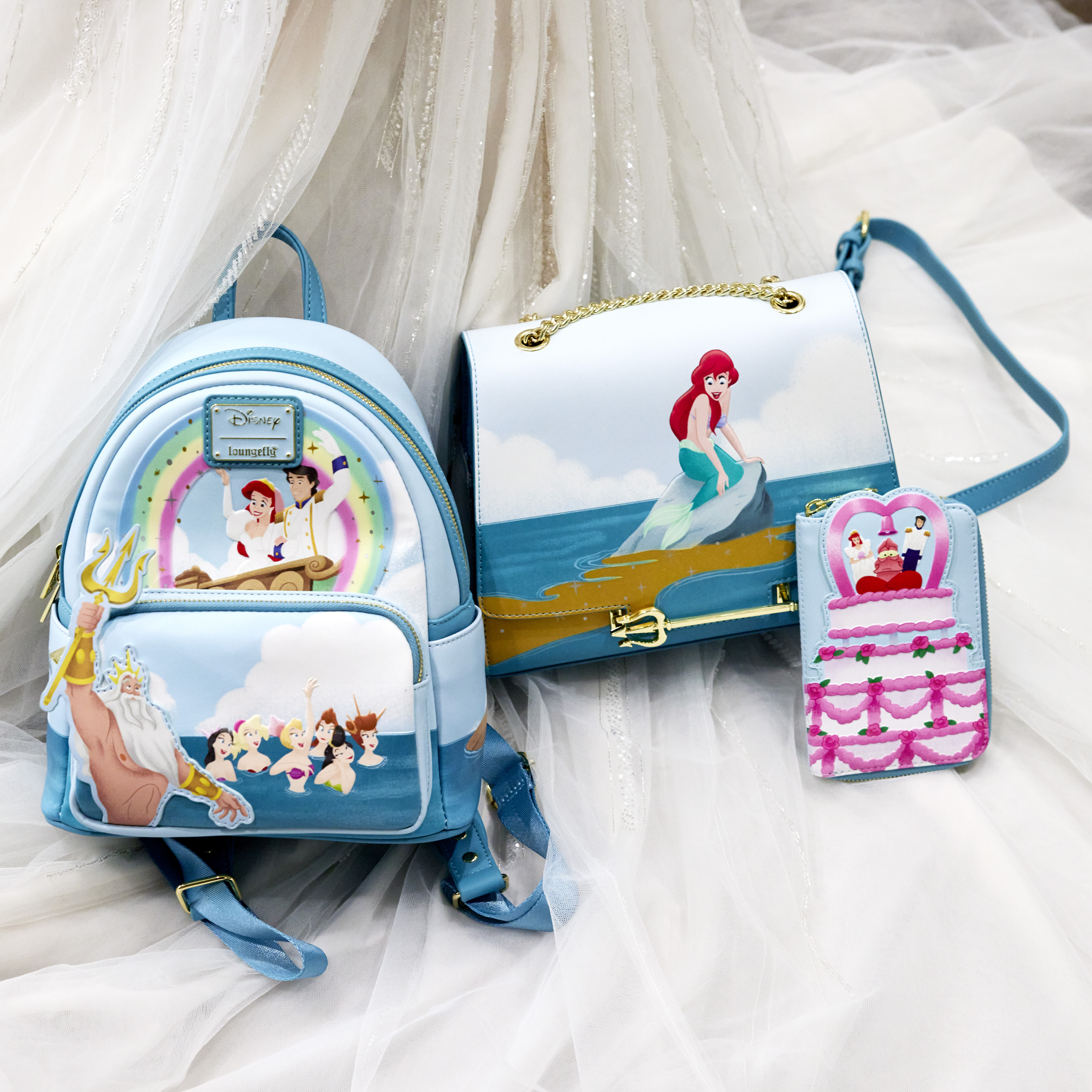 The Little Mermaid Triton's Gift Mini Backpack and Crossbody Bag, and Ariel Wedding Cake Zip Around Wallet sitting atop the bottom of a wedding gown